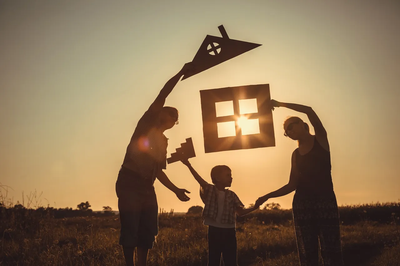 Happy family standing on the field at the sunset time. They build a house. Concept of friendly family.